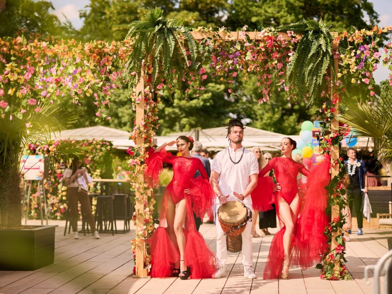 group of dancers in red skirts and a percussionist under an arch of flowers at an event