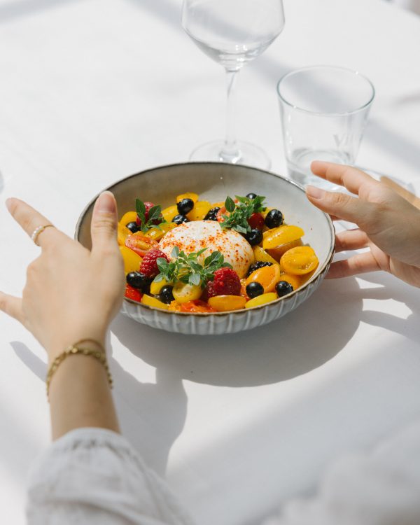 assiette avec une buratta acoompagnée de fruits frais, dressée sur une table dans un restaurant extérieur